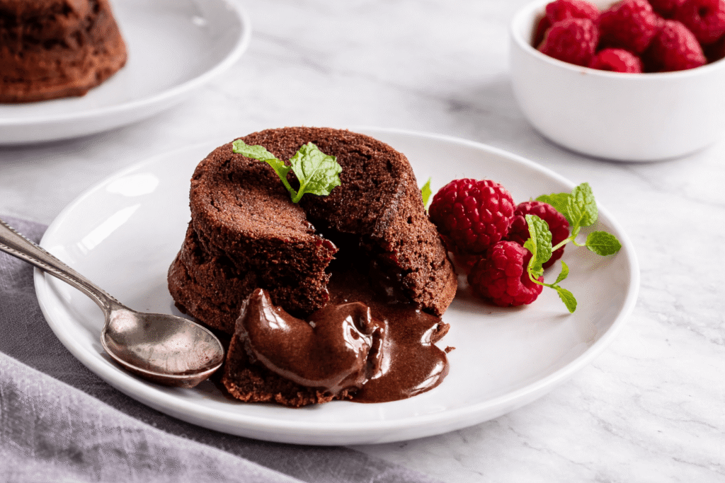 Gooey Chocolate Lava Brookie Cake with rich molten chocolate oozing from the center, garnished with fresh mint leaves and served with sweet raspberries on a white plate
